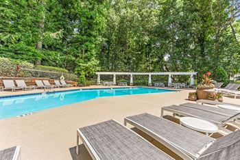 A pool surrounded by trees and lounge chairs.
